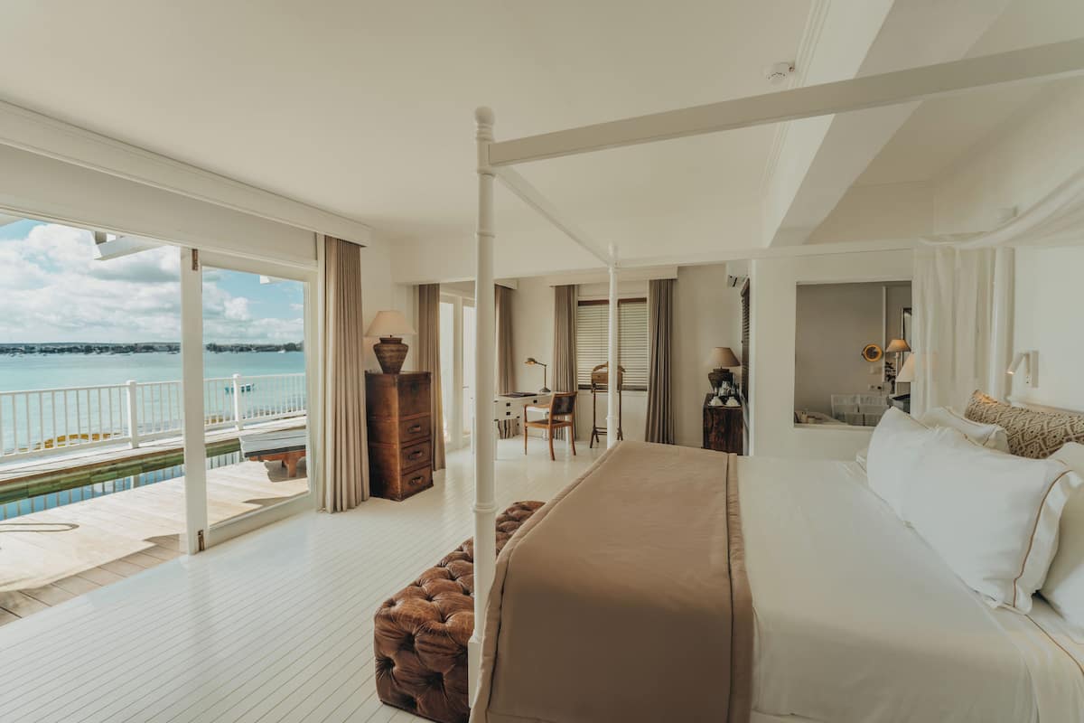 A bedroom with a large bed, a view of the sea, a balcony, and a desk with a chair.