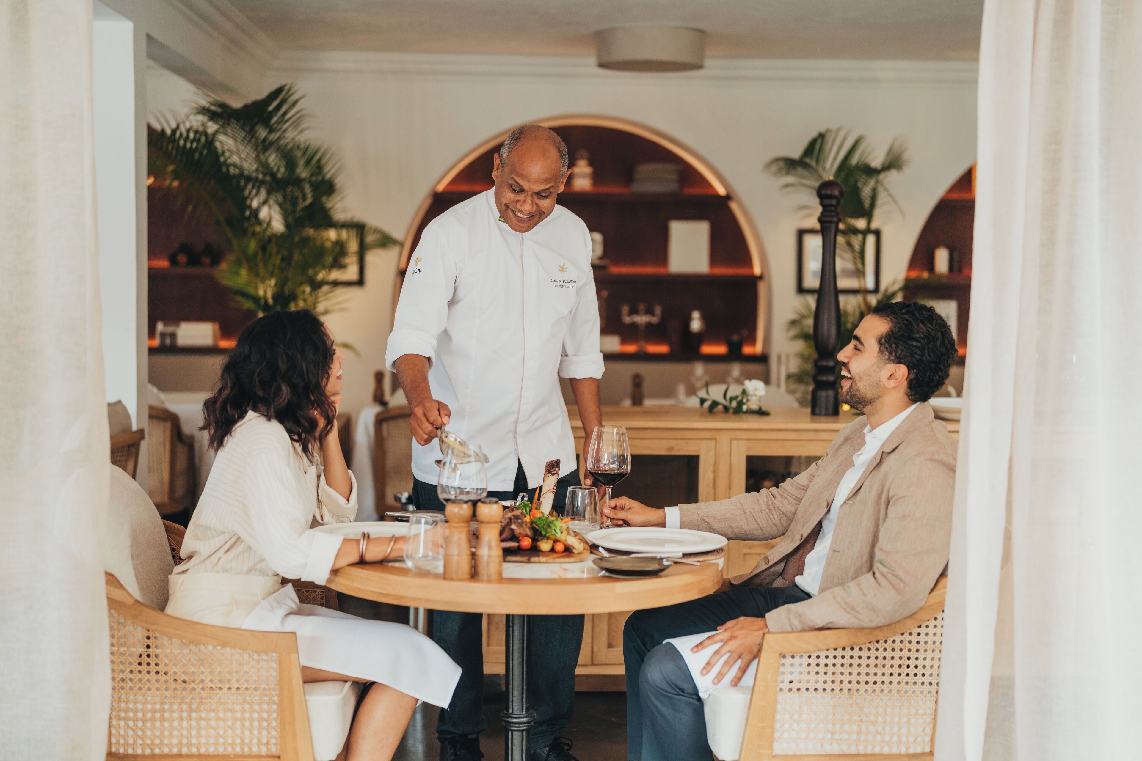 A dining area with a round table, chairs, and a waiter serving food.