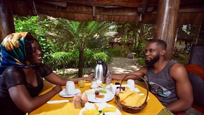 Une table à manger avec des assiettes remplies de nourriture, une cafetière et un panier de pain.