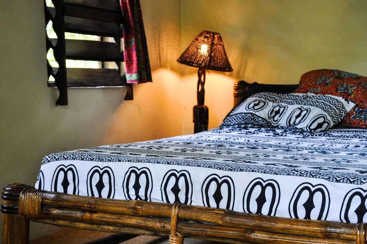 Una cama con colcha estampada, cabecera de madera, lámpara de noche y repisa de pared con tela estampada.