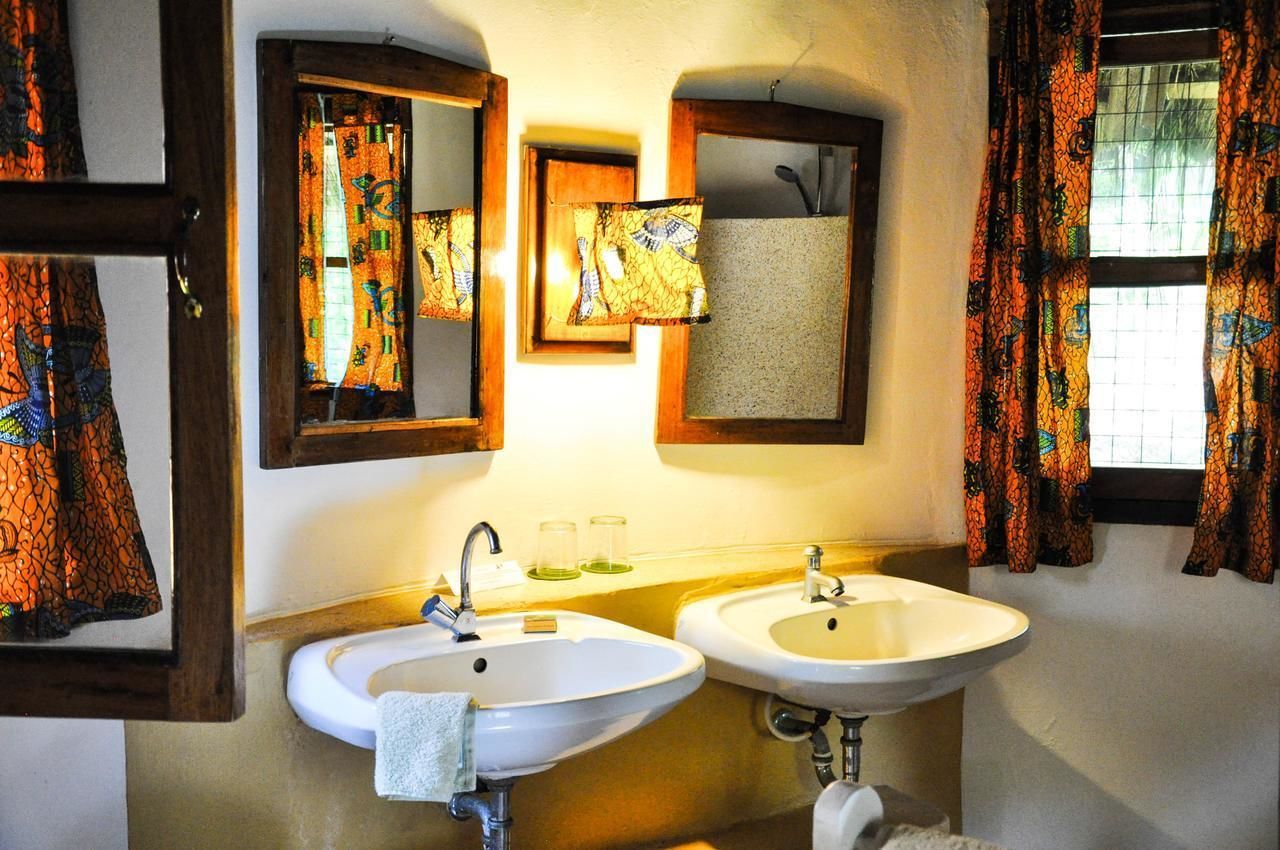 Un baño con dos lavamanos, un espejo y un ventanal con cortinas.