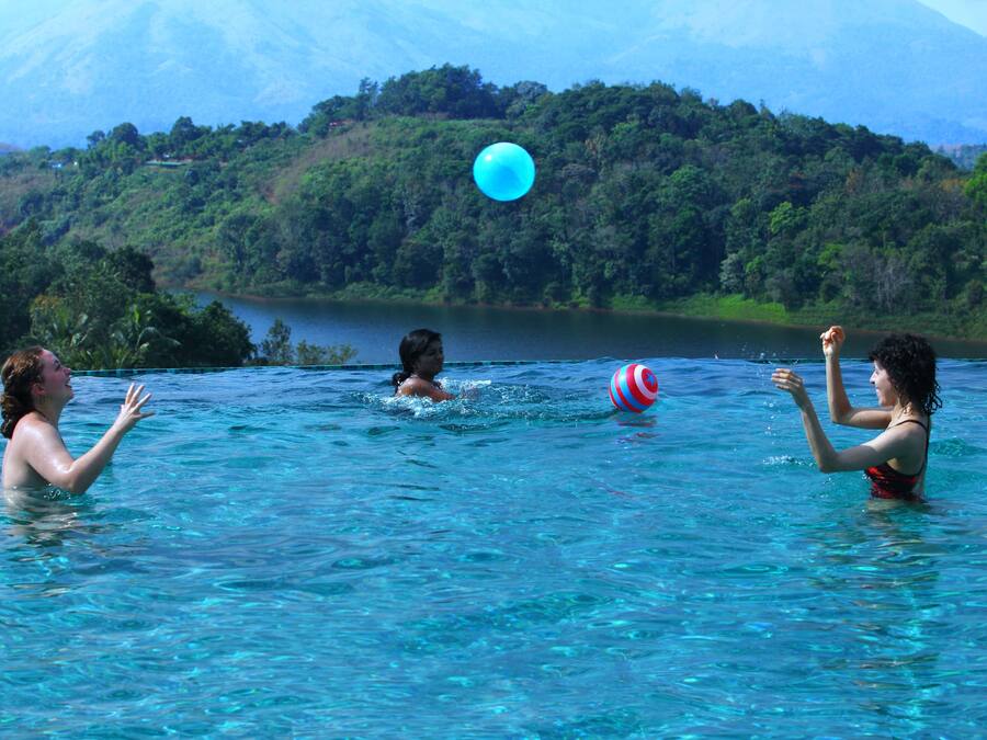 A group of people playing with a ball in a clear blue body of water, surrounded by lush greenery and hills in the background.