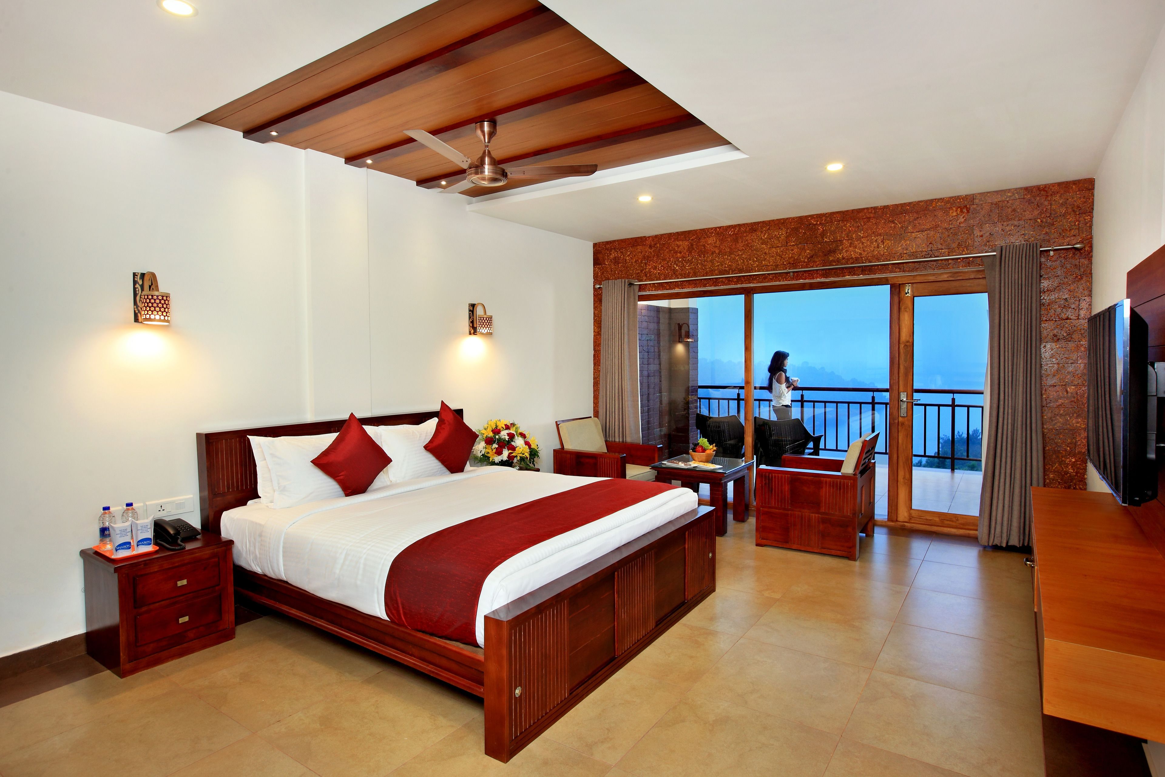 A hotel room with a large bed, a desk, a chair, a TV, and a balcony with a view.