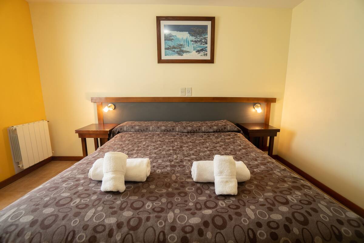 Una habitación de hotel con una cama grande, dos mesitas de noche, un cabecero y un cuadro en la pared.