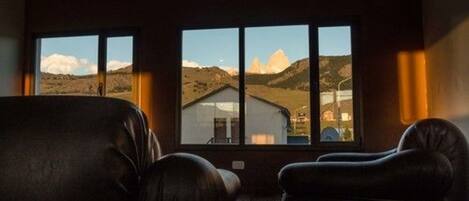 Una habitación con un ventanal amplio que ofrece vistas a un paisaje montañoso y un edificio. Hay dos sillones de cuero en la habitación.
