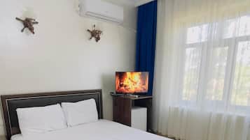 A hotel room with a bed, a TV, an air conditioning unit, and a window with curtains.