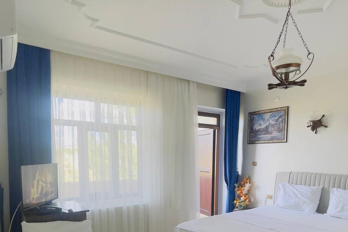 Hotellihuone, jossa on kaksi sänkyä, kattotuuletin, taulu ja ikkuna, jossa on verhot.
