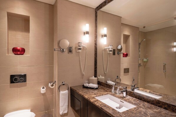 Un baño moderno con lavamanos de mármol, espejos dobles, cabezal de ducha de mano y un perchero para toallas.