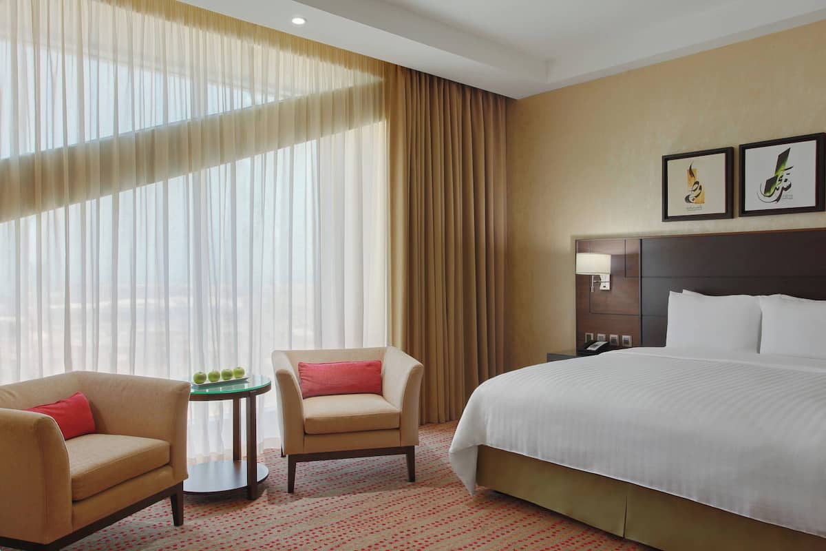 A hotel room with a bed, two armchairs, a small table with apples, a nightstand, and curtains.