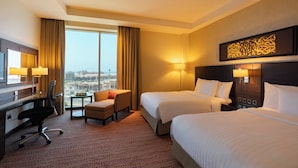 Habitación de hotel con dos camas, un escritorio, una silla y vistas a la ciudad.