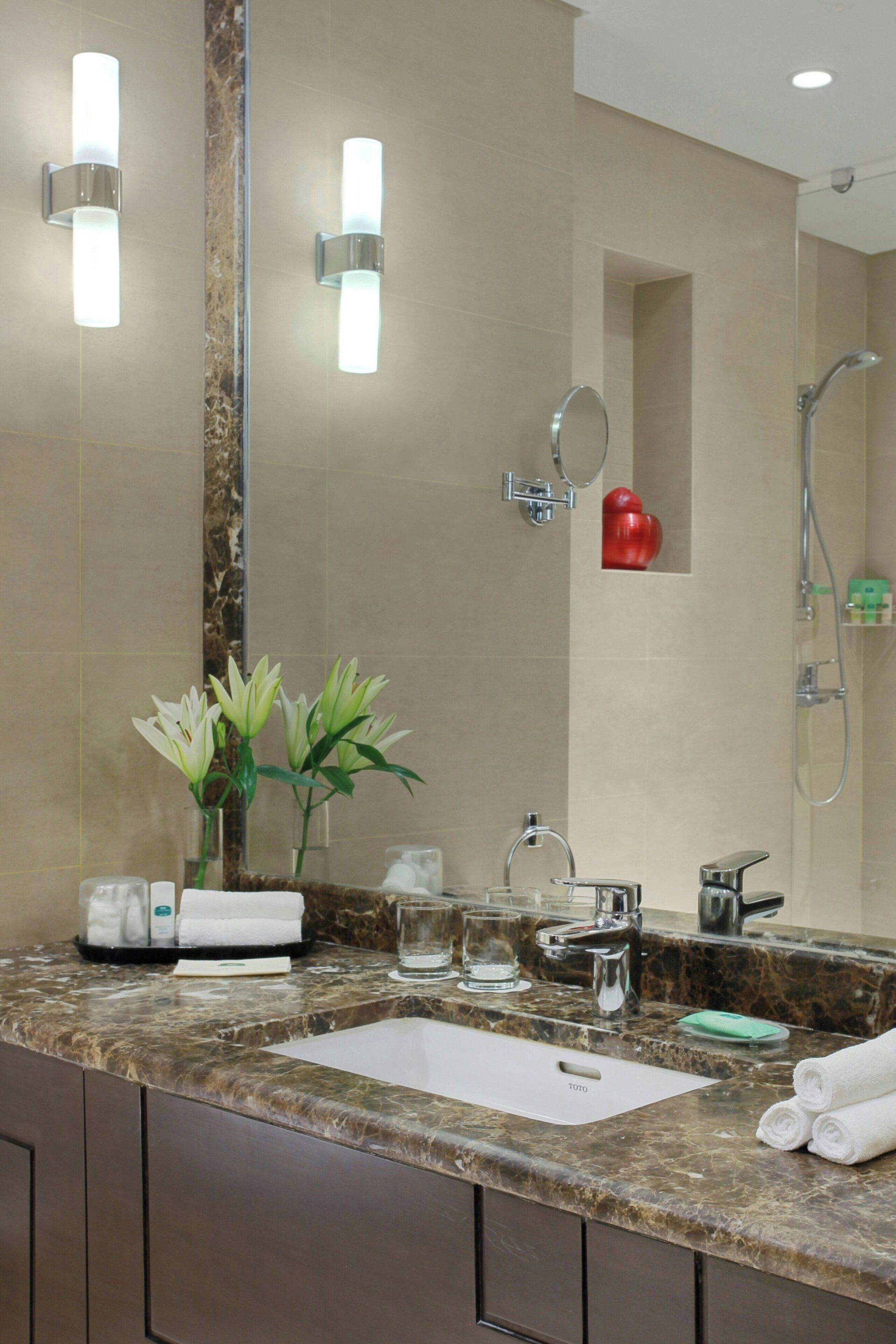 A bathroom with a marble sink, a mirror, a handheld showerhead, and a red heart-shaped decoration on the wall.