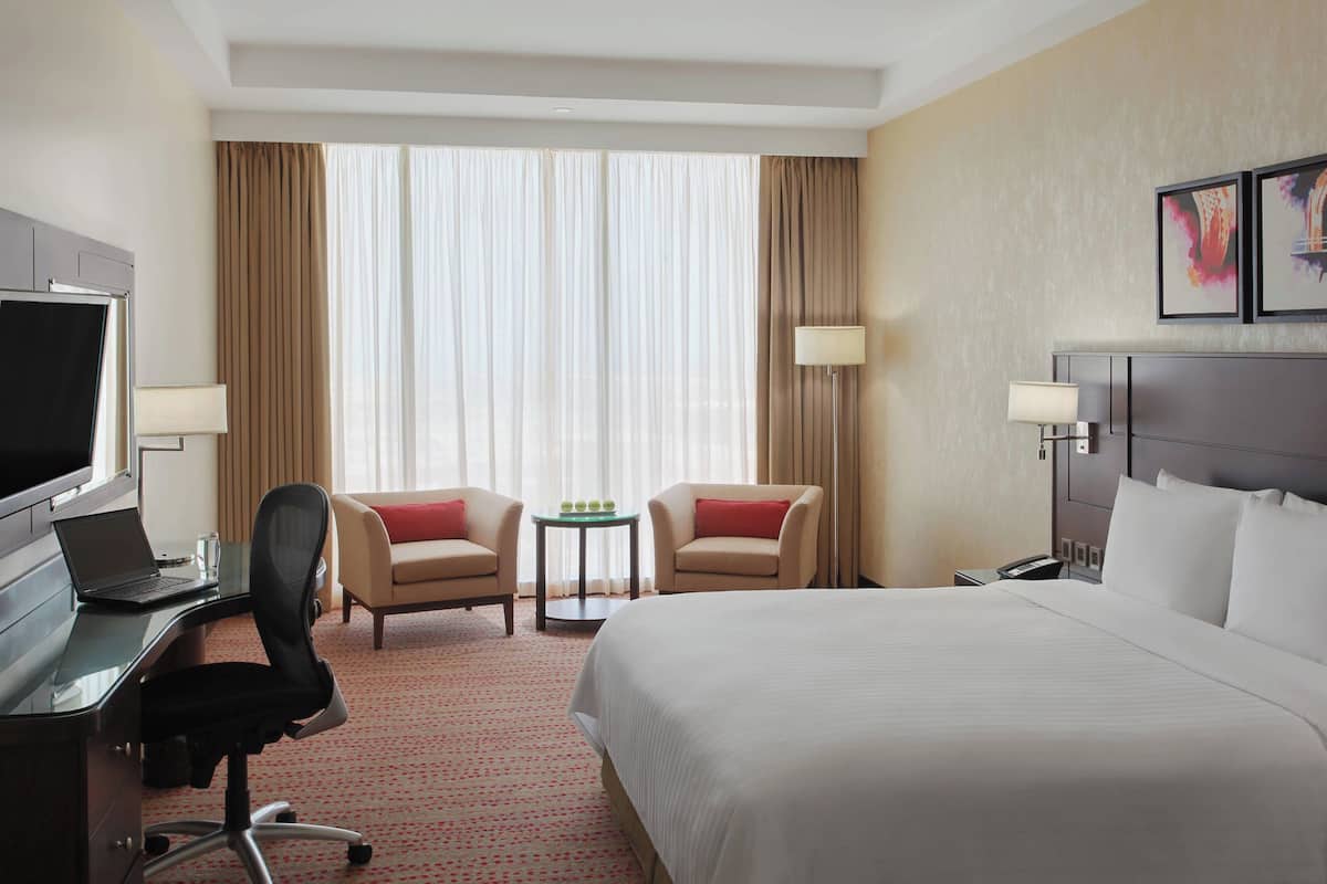 A hotel room with a bed, desk, two chairs, a TV, and a small table with a lamp.
