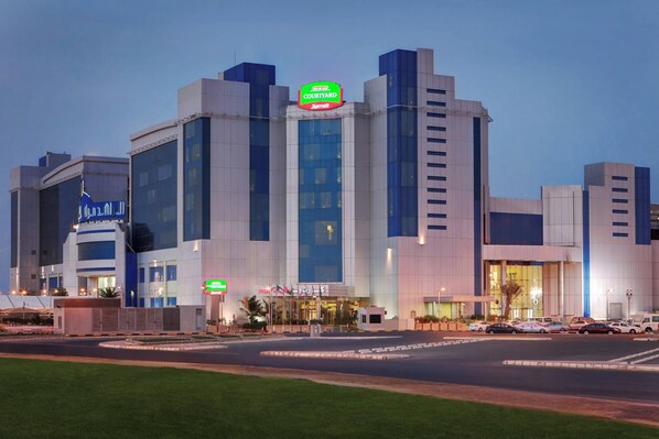 A multi-story hotel with a prominent Courtyard by Marriott sign, large windows, and a parking area with several cars.