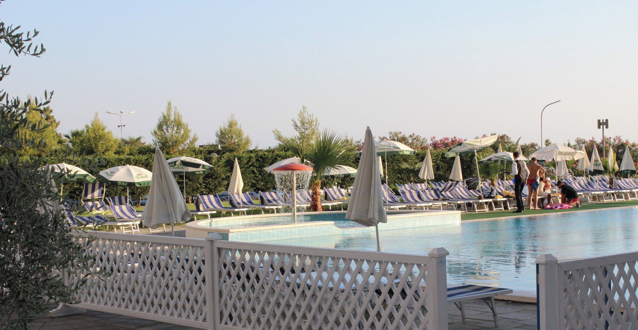 A pool area with lounge chairs and umbrellas, surrounded by trees and a fence.