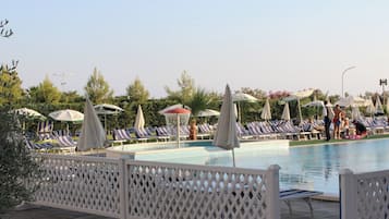 A pool area with lounge chairs and umbrellas, surrounded by trees and a fence.