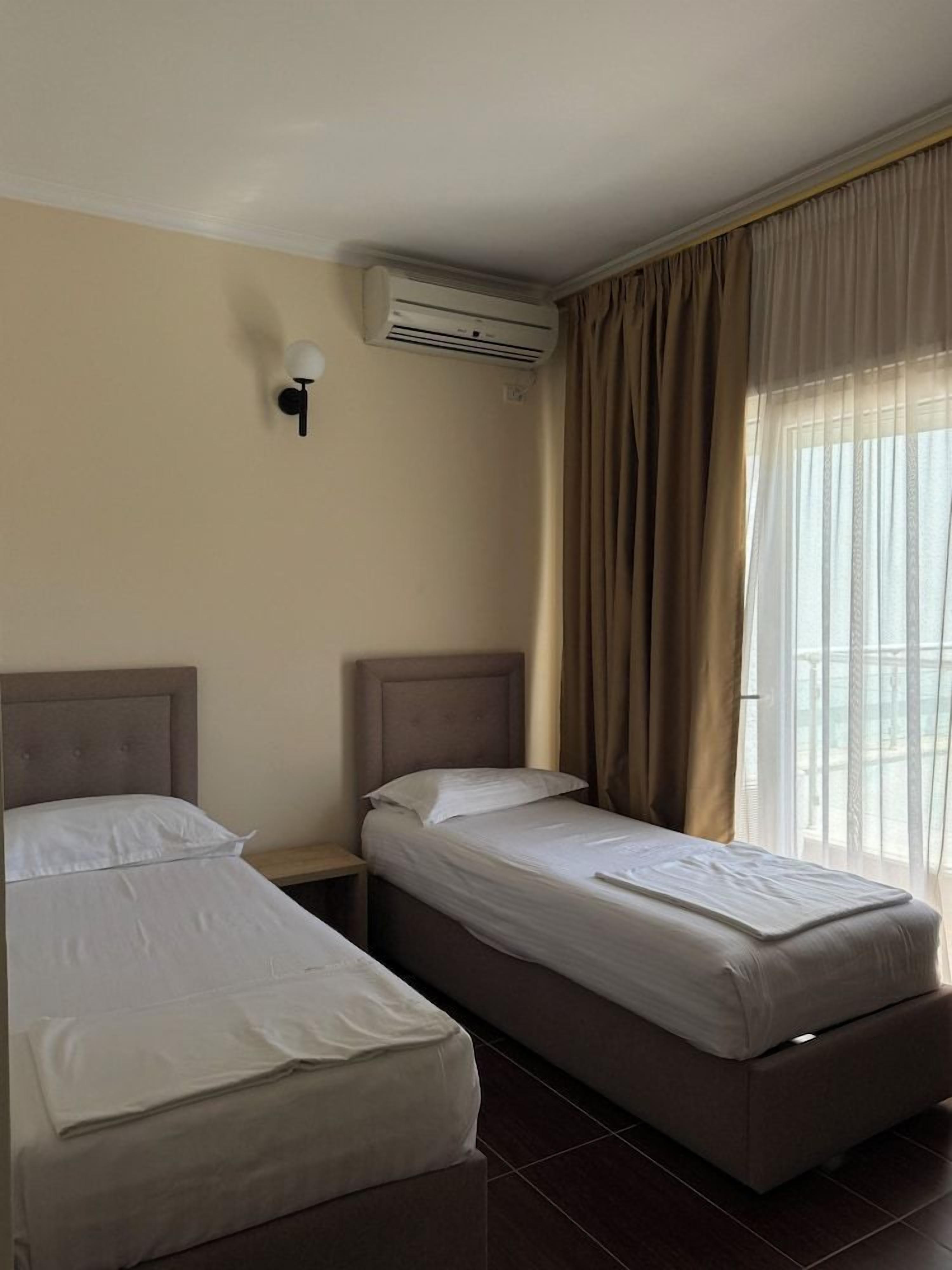 Une chambre d’hôtel avec deux lits, un climatiseur fixé au mur et une fenêtre avec des rideaux.