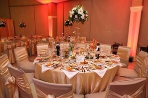 A banquet hall with round tables set for dining, chairs with white covers, and floral centerpieces. - Bleart (Rrashbull)