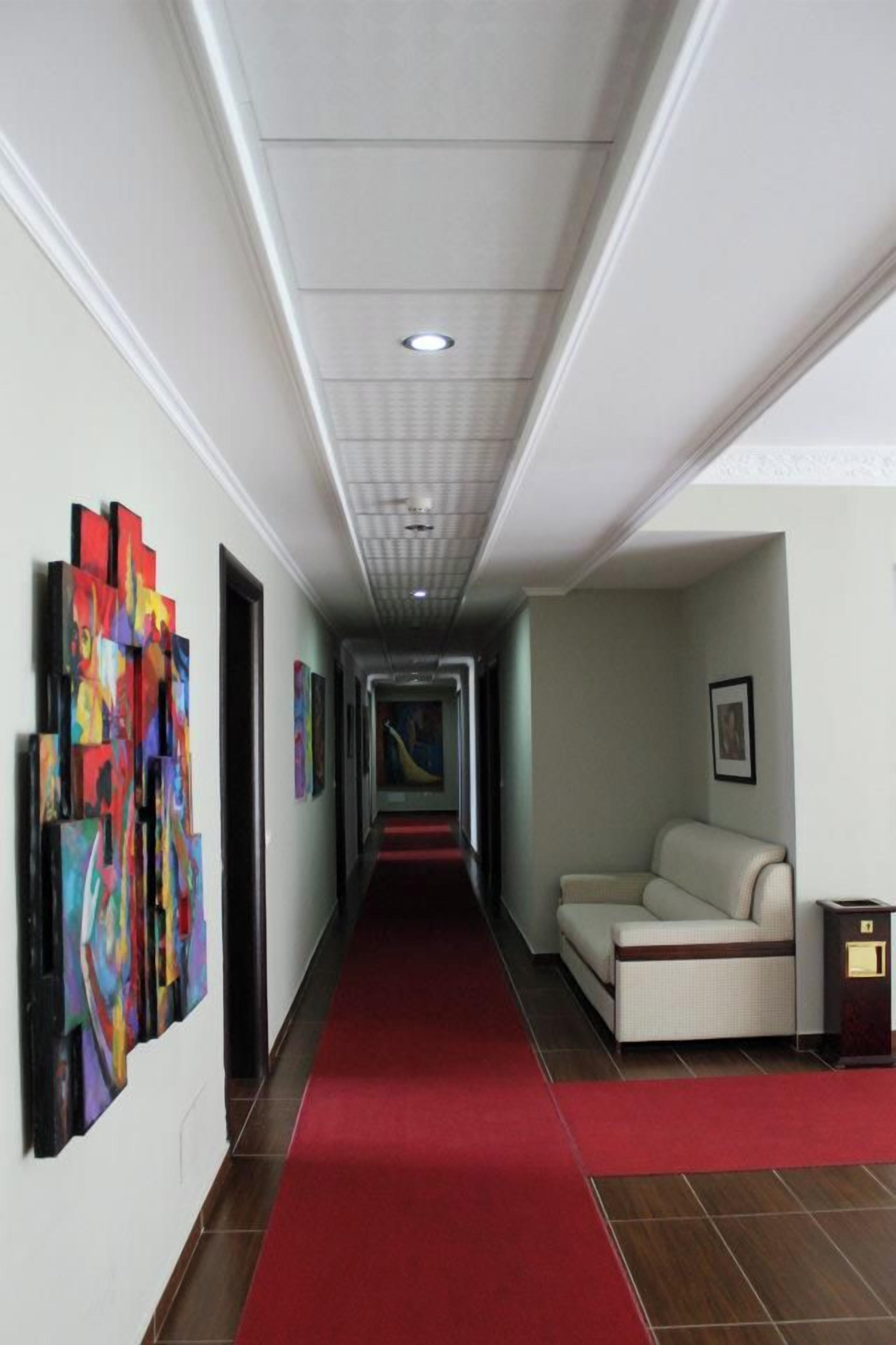 A hotel hallway with a red carpet, a sofa, and colorful artwork on the walls.