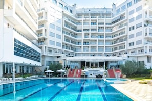 Un hôtel à plusieurs étages doté d’un espace piscine central, de sièges en plein air et d’une terrasse couverte.