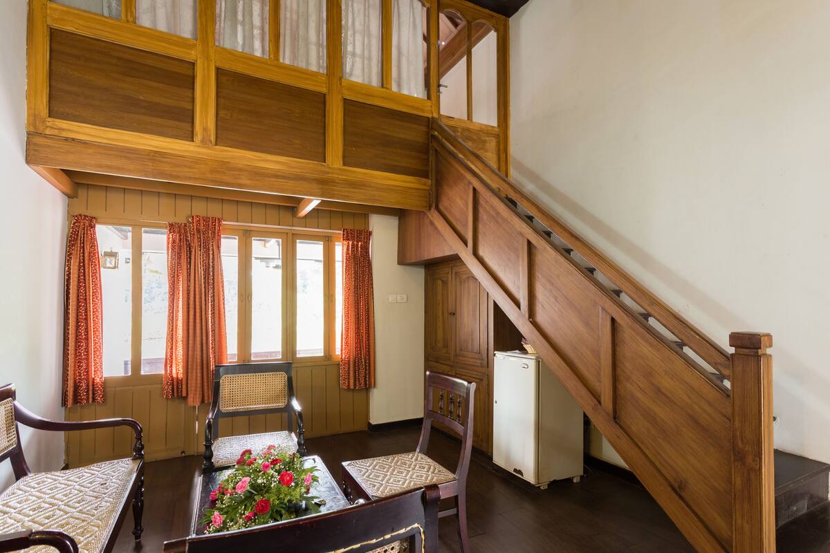 Una escalera de madera que conduce a un nivel superior, un comedor con mesa y sillas, y un refrigerador pequeño.