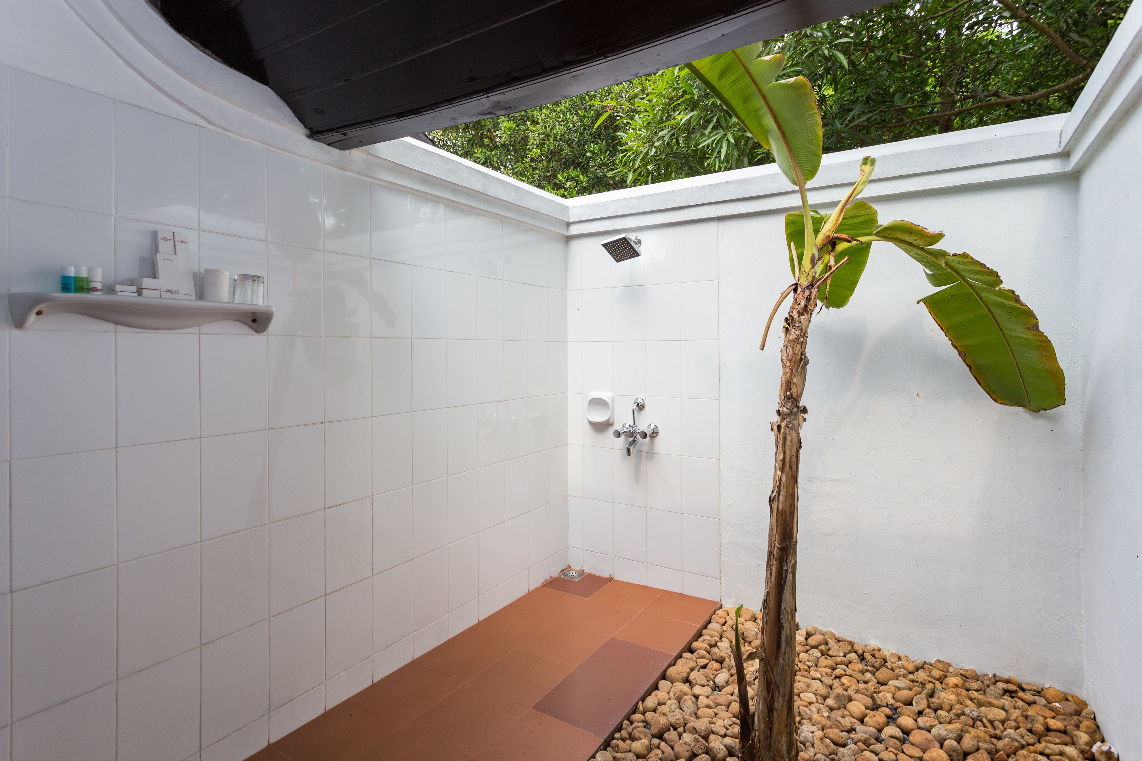 Un espacio de ducha pequeño y cerrado, con paredes de azulejos blancos, piso marrón y un estante con artículos de tocador.