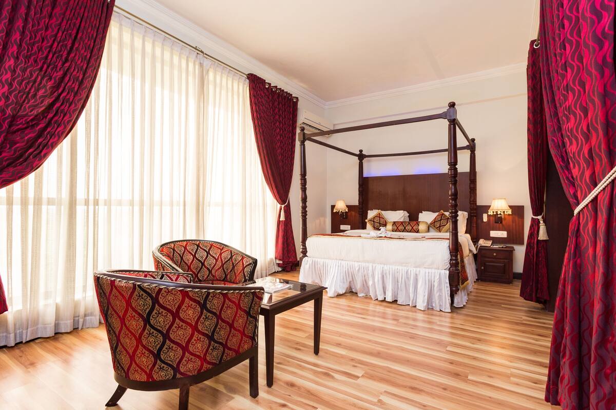Una cama con dosel, una silla, una mesita de noche y un velador en una habitación de hotel.