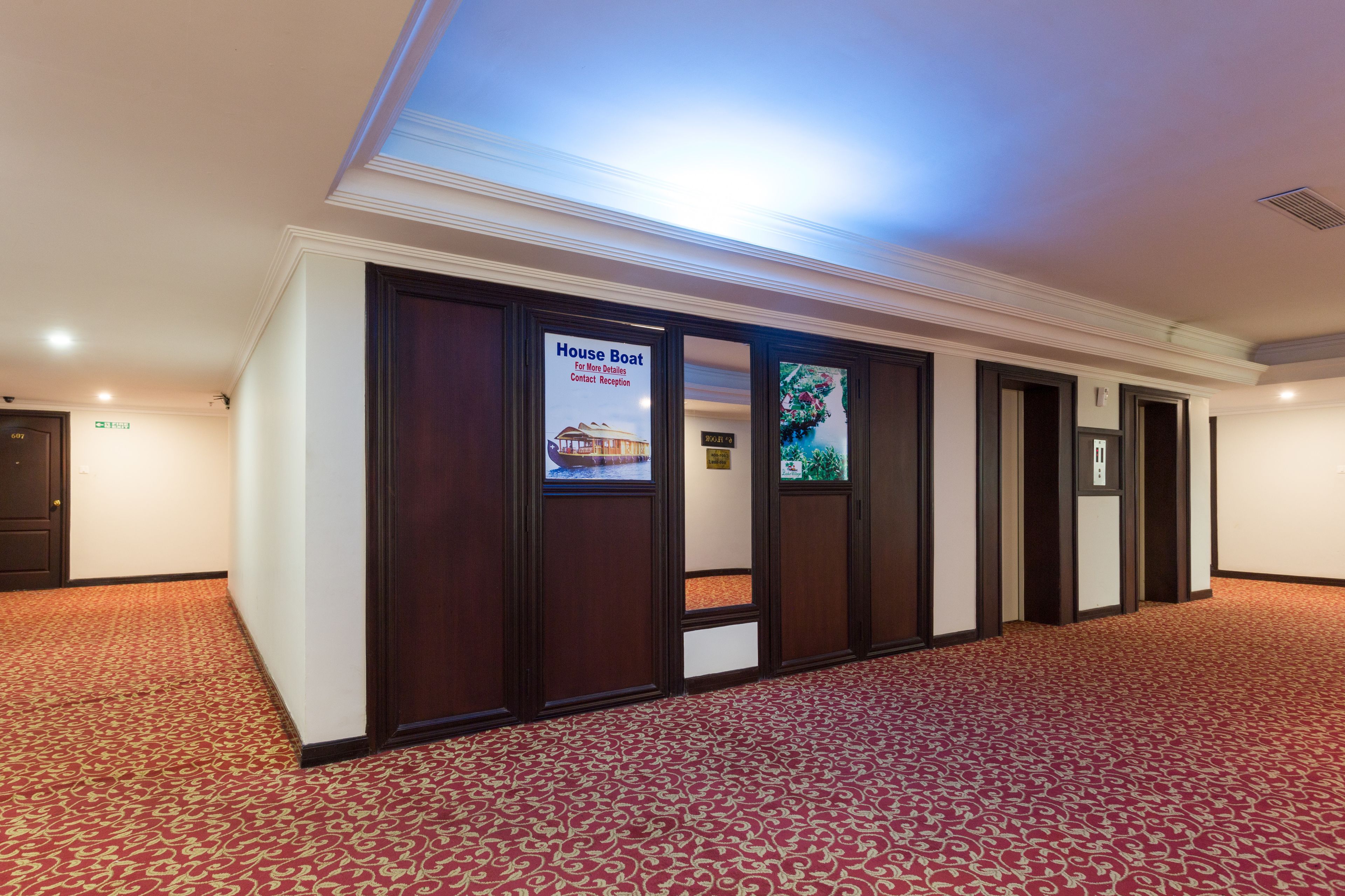 A hotel hallway with a red patterned carpet, wooden paneling, and a sign for the House Boat contact reception.