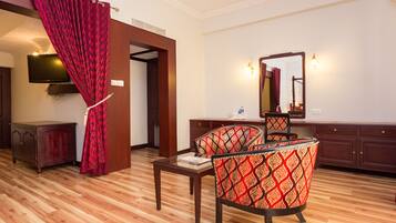 Quarto de hotel com piso de madeira, cortina vermelha, televisão, espelho e escrivaninha com cadeira.