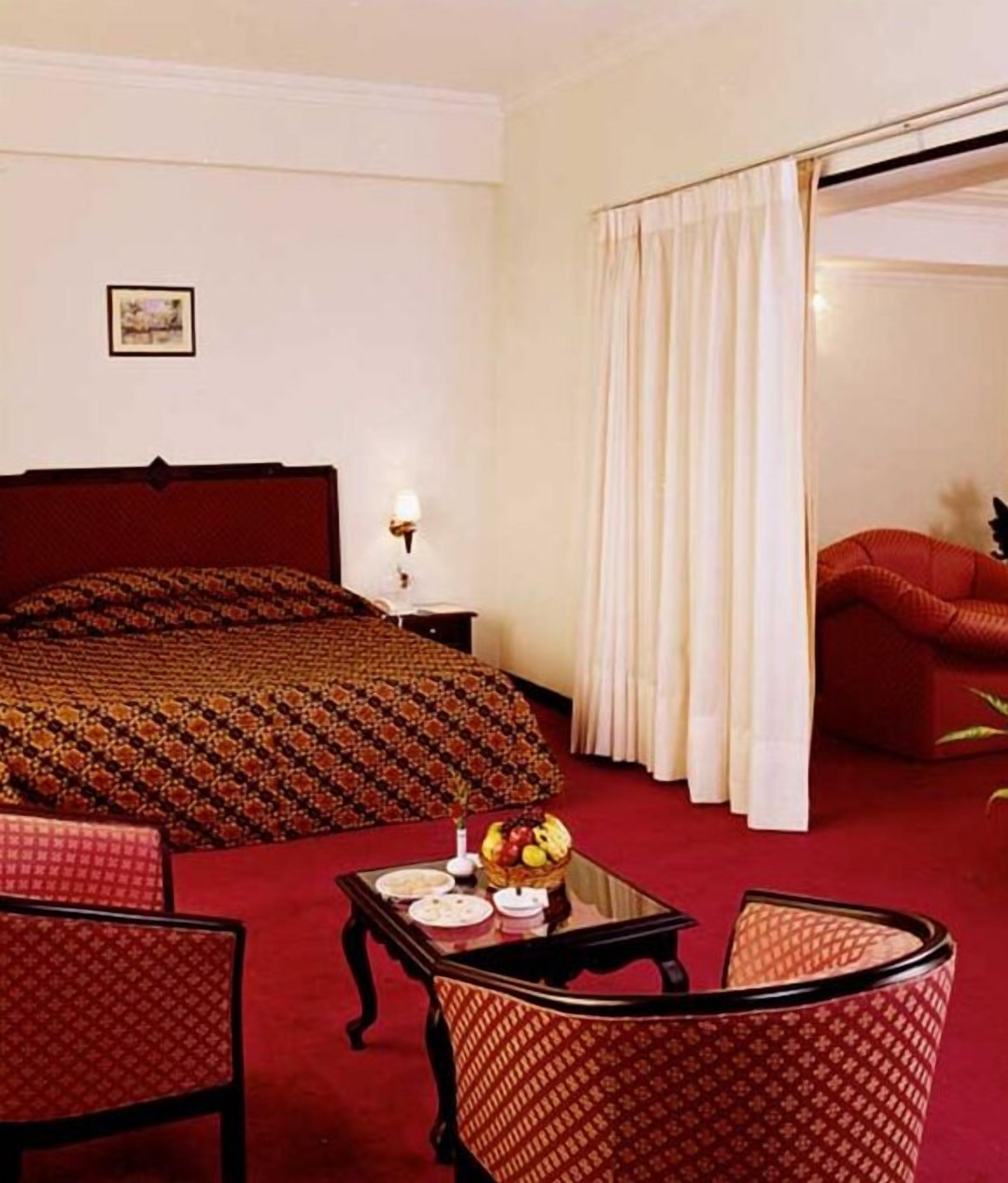 Una habitación de hotel con una cama grande, una zona de estar con una mesa y sillas, y una ventana con cortinas.
