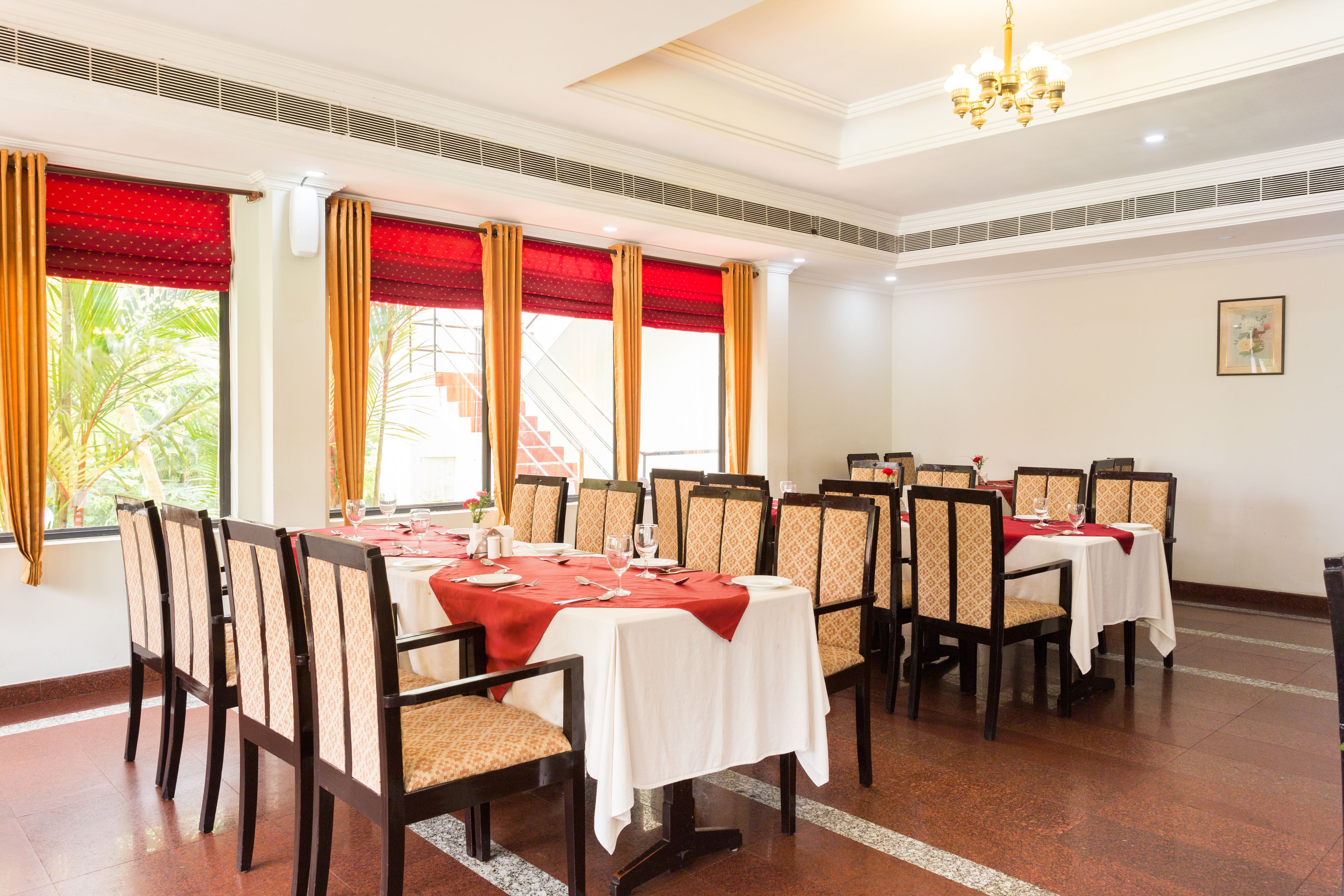 Ein Essbereich mit Tischen für sechs Personen, jeder Tisch mit roter Tischdecke und weißen Tischläufern. Die Stühle sind mit gemusterten Kissen ausgestattet.