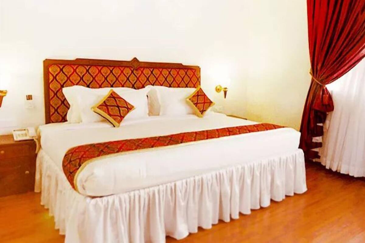 Una cama bien hecha, con un cabecero estampado, ropa de cama blanca y un corredor de cama rojo y blanco.