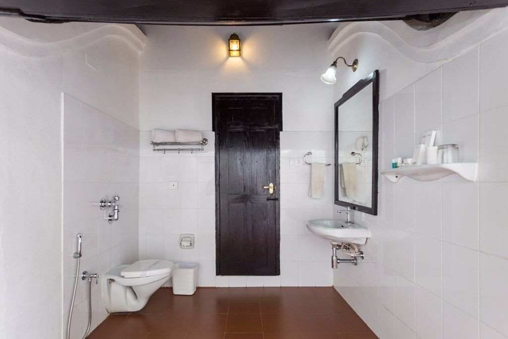 Une salle de bain équipée de toilettes, d’un lavabo et d’une douche. On trouve un porte-serviettes au-dessus des toilettes et un miroir au-dessus du lavabo.