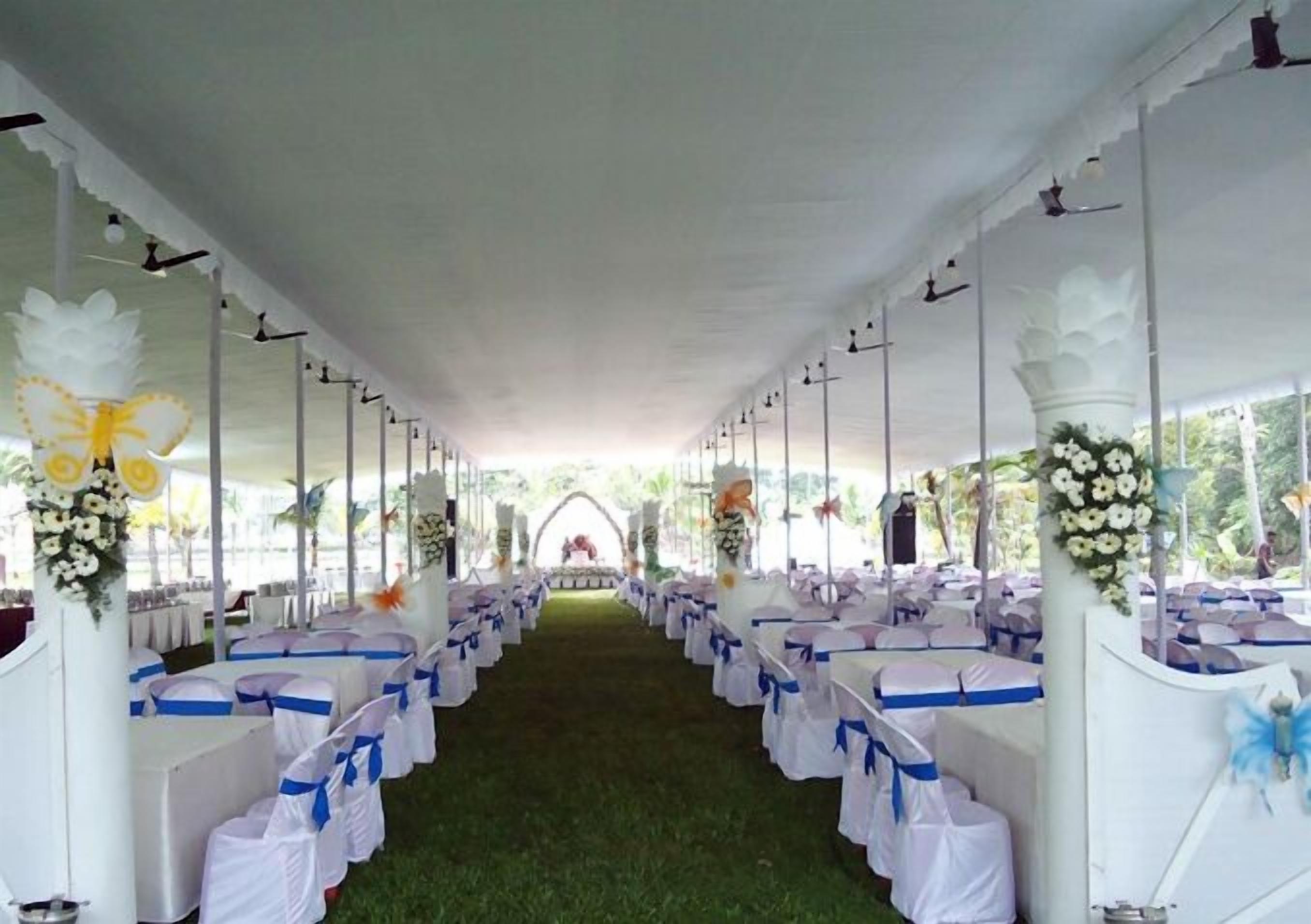A tented wedding venue with rows of tables and chairs, decorated with floral arrangements and blue sashes.