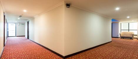 A hotel corridor with a red carpet, white walls, and a beige sofa in the corner.
