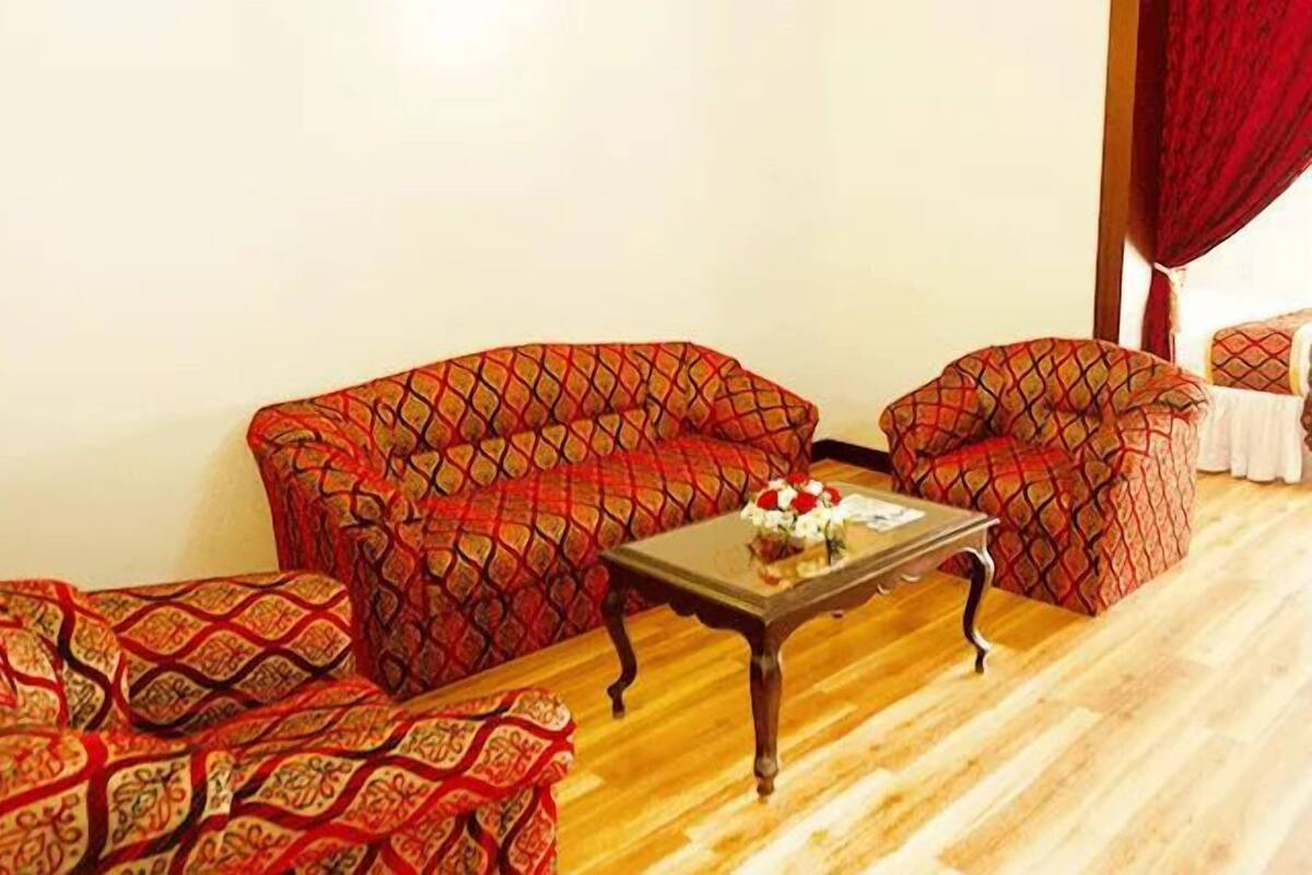Una habitación con dos sillones estampados, una mesa de centro de madera y una mesita con un florero.