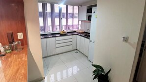 A compact kitchen with white cabinets, a black countertop, and a window providing natural light. - Lorenzo Suites Hotel (San Miguel de Tucuman)