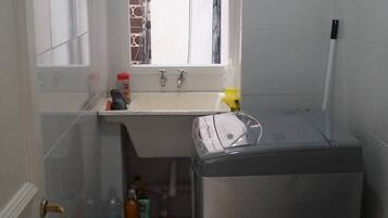 A small, compact kitchen with a window above the sink, a refrigerator, and a countertop with various items.