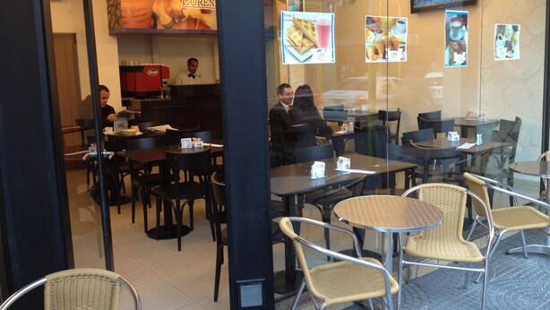 A restaurant with tables and chairs, a counter with a person behind it, and menu boards on the wall. - Lorenzo Suites Hotel (San Miguel de Tucuman)