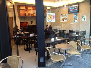 A restaurant with tables and chairs, a counter with a person behind it, and menu boards on the wall. - Lorenzo Suites Hotel (San Miguel de Tucuman)