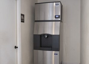 A stainless steel refrigerator with a water dispenser and a digital display, located in a hallway with a door and a sign indicating restrooms. - Red Roof Inn Lancaster - Strasburg (Lancaster)