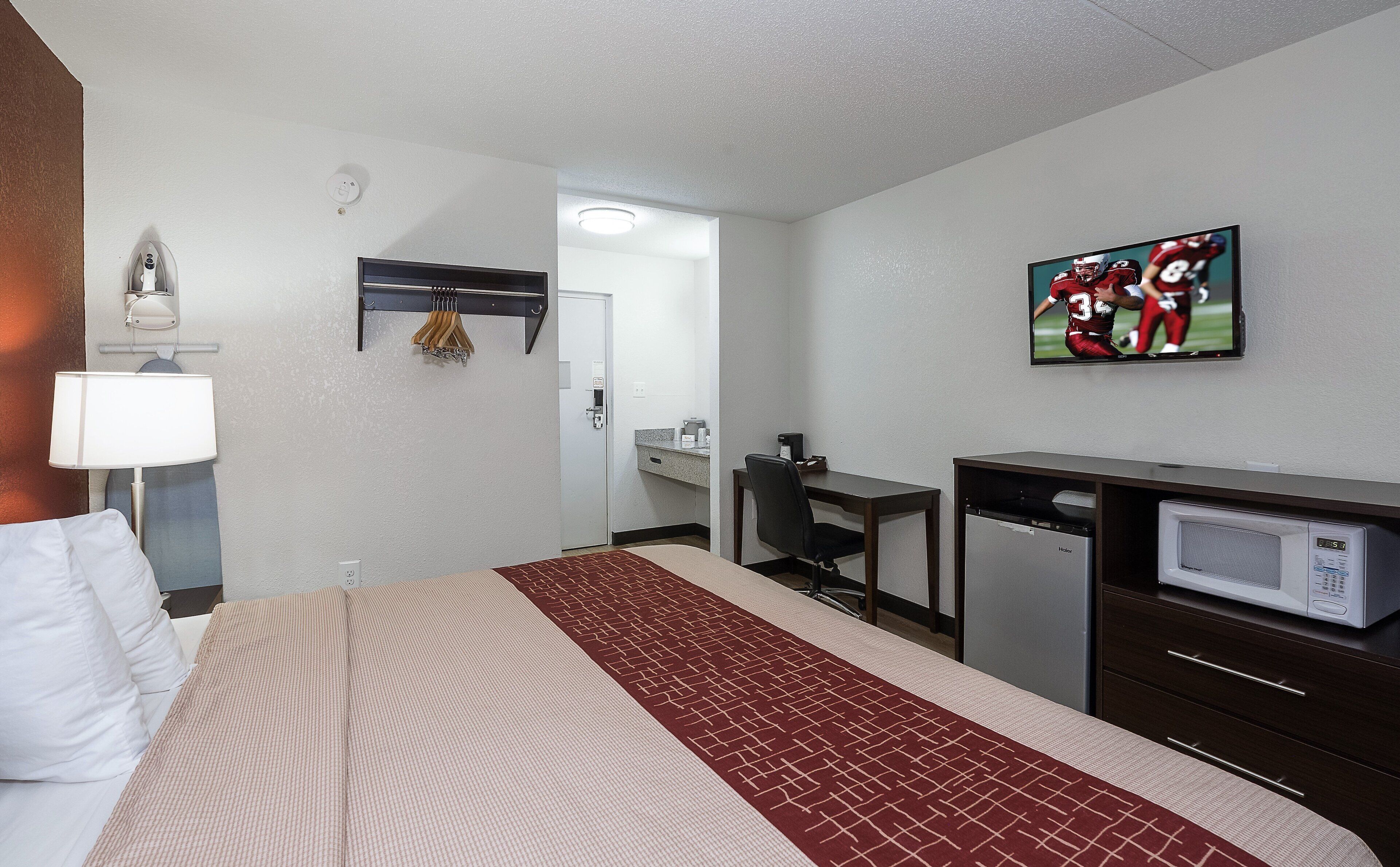 A hotel room with a bed, a desk, a microwave, a television, and a painting on the wall.