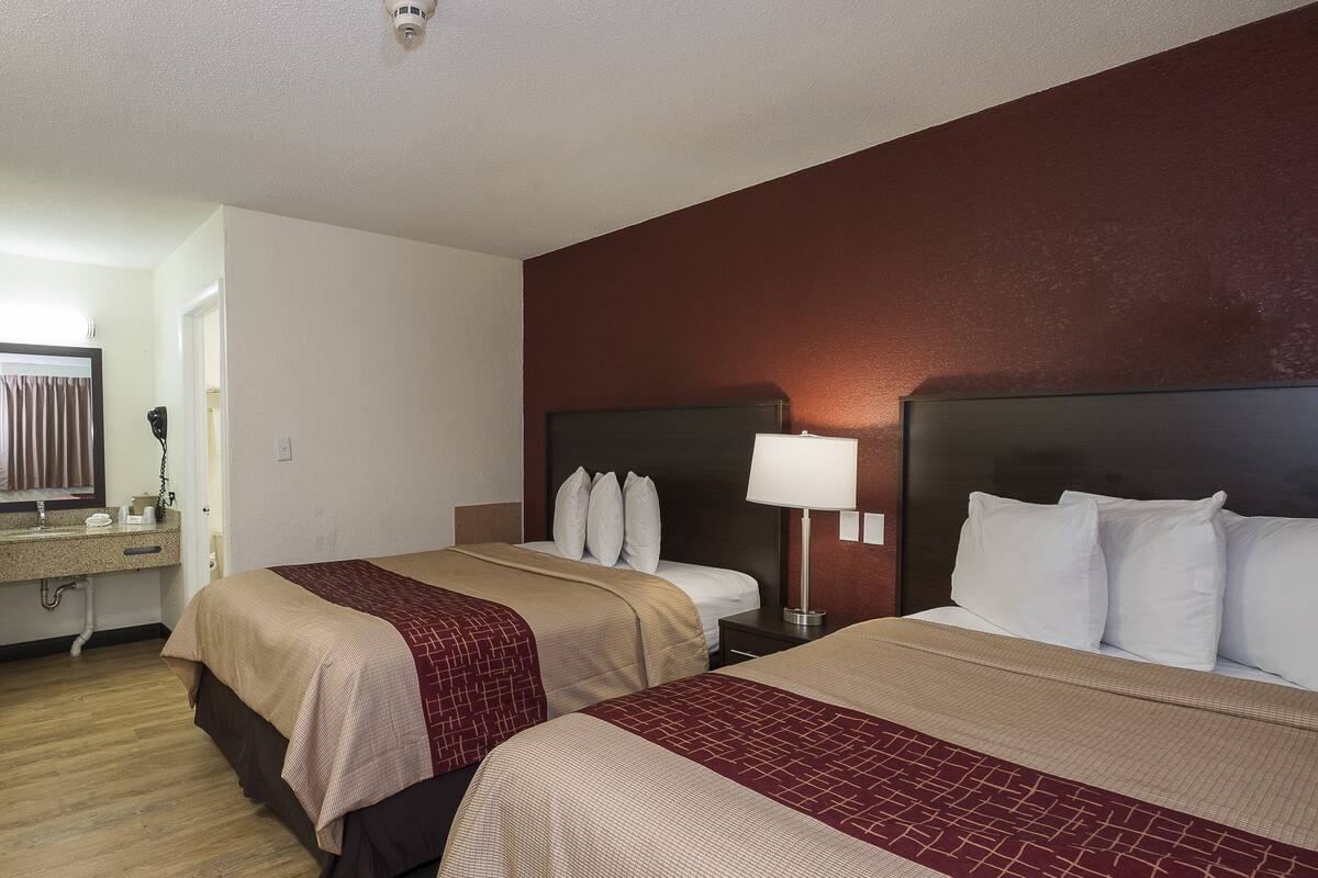 A hotel room with two beds, a bathroom, and a nightstand with a lamp.