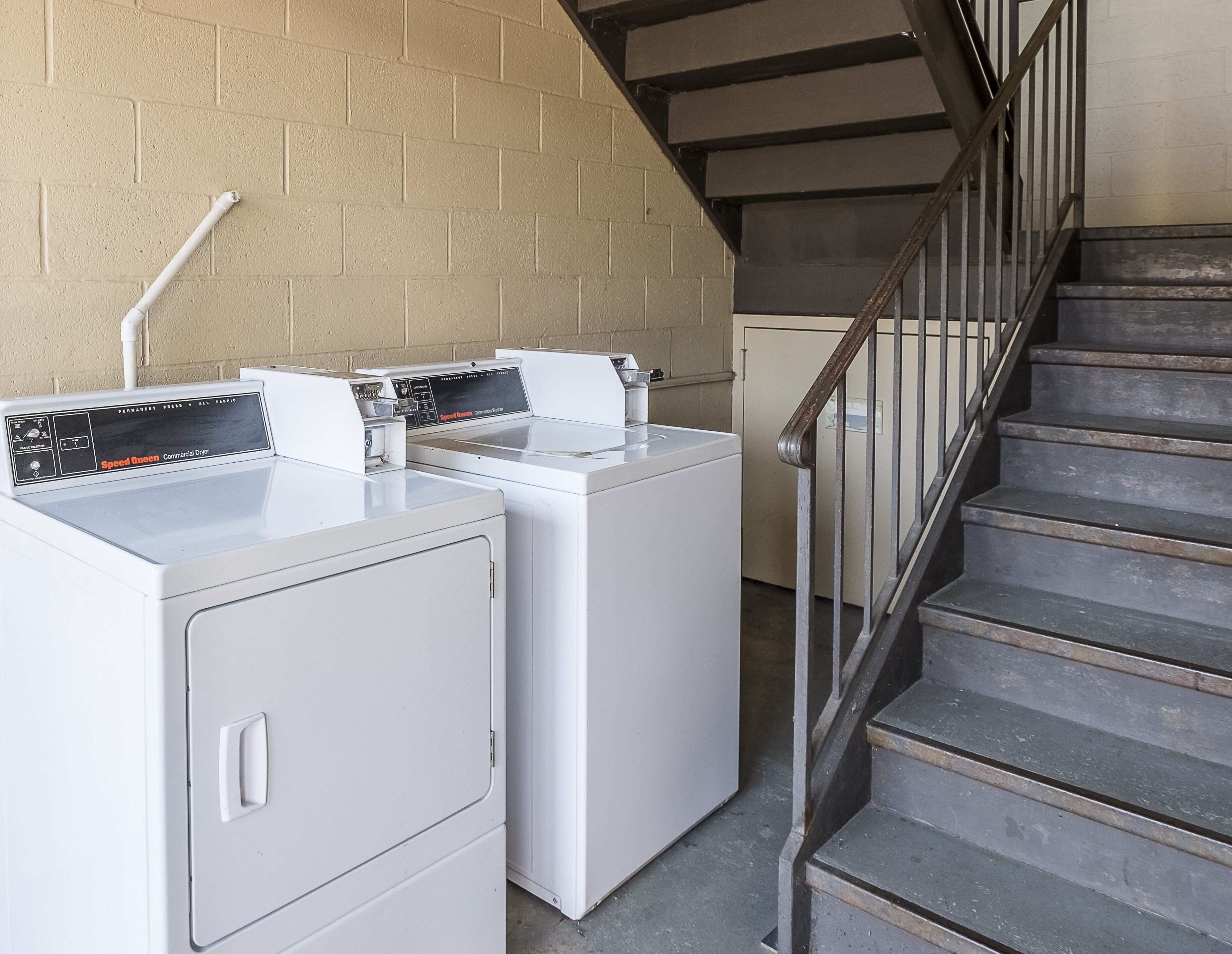 A laundry area with two white commercial dryers and a metal staircase.