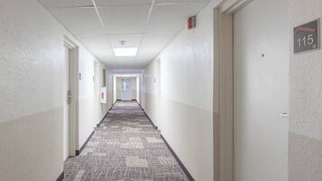 A hotel hallway with carpeted floors, white walls, and doors numbered 115.
