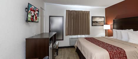 A hotel room with a bed, a desk, a chair, a television, a window with curtains, and a wall-mounted picture.