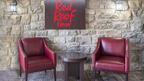 A Red Roof Inn sign on a stone wall with two red leather chairs and a small round table. - Red Roof Inn Lancaster - Strasburg (Lancaster)