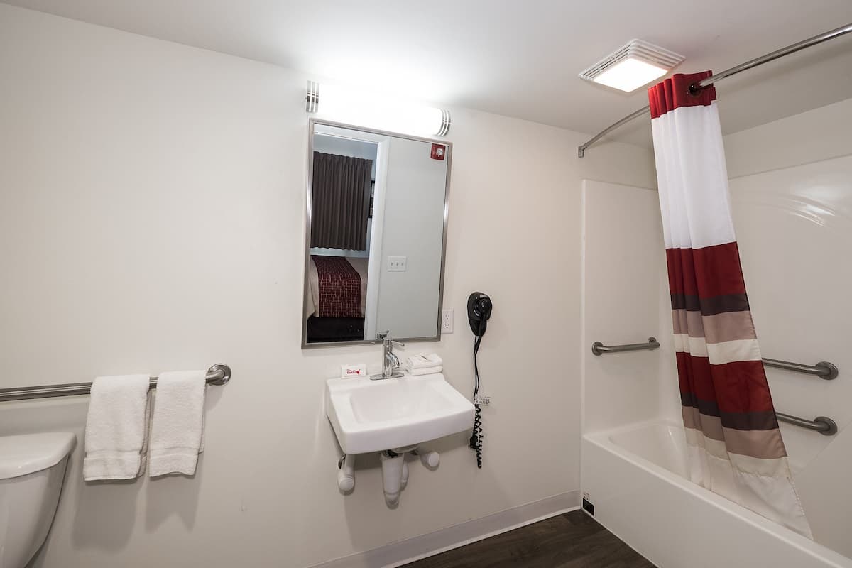 A bathroom with a white sink, a mirror, a towel rack, a shower with a striped curtain, and a handheld hairdryer.
