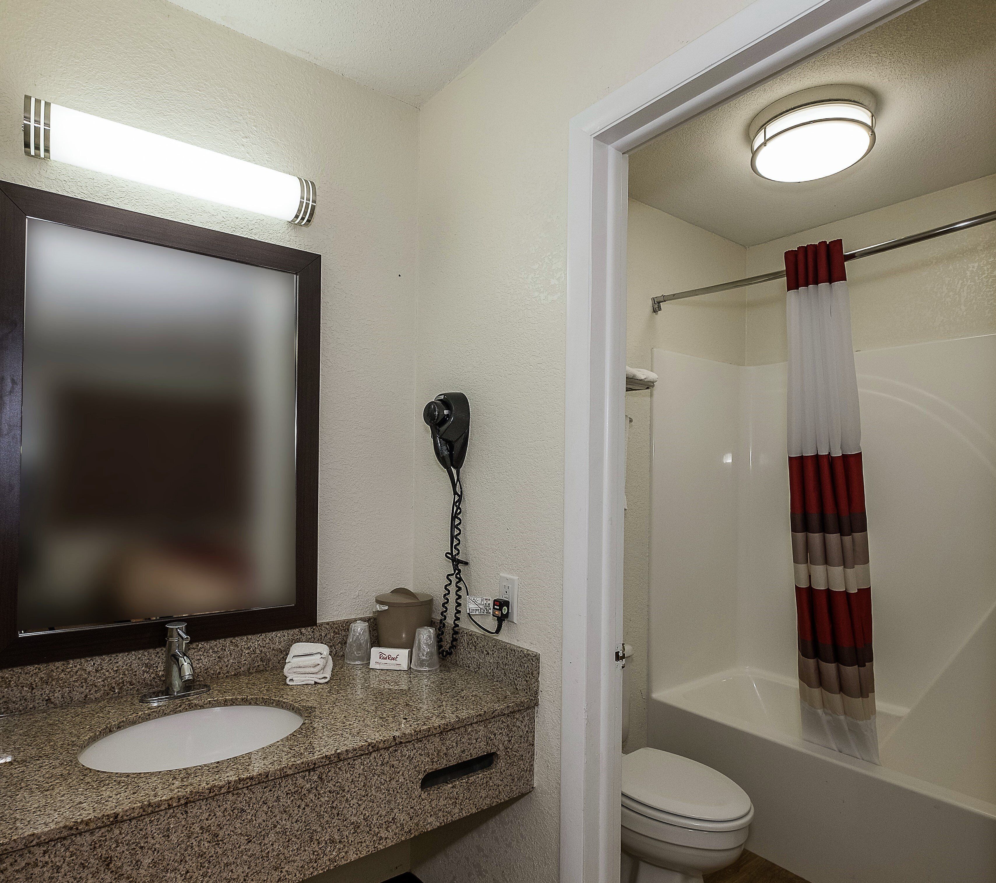 Une salle de bain avec un comptoir en granit, un miroir, un sèche-cheveux, une serviette et un rideau de douche.