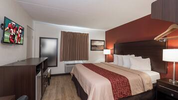 A hotel room with a bed, a desk, a TV, a window with curtains, a wall-mounted picture, and a bedside lamp.