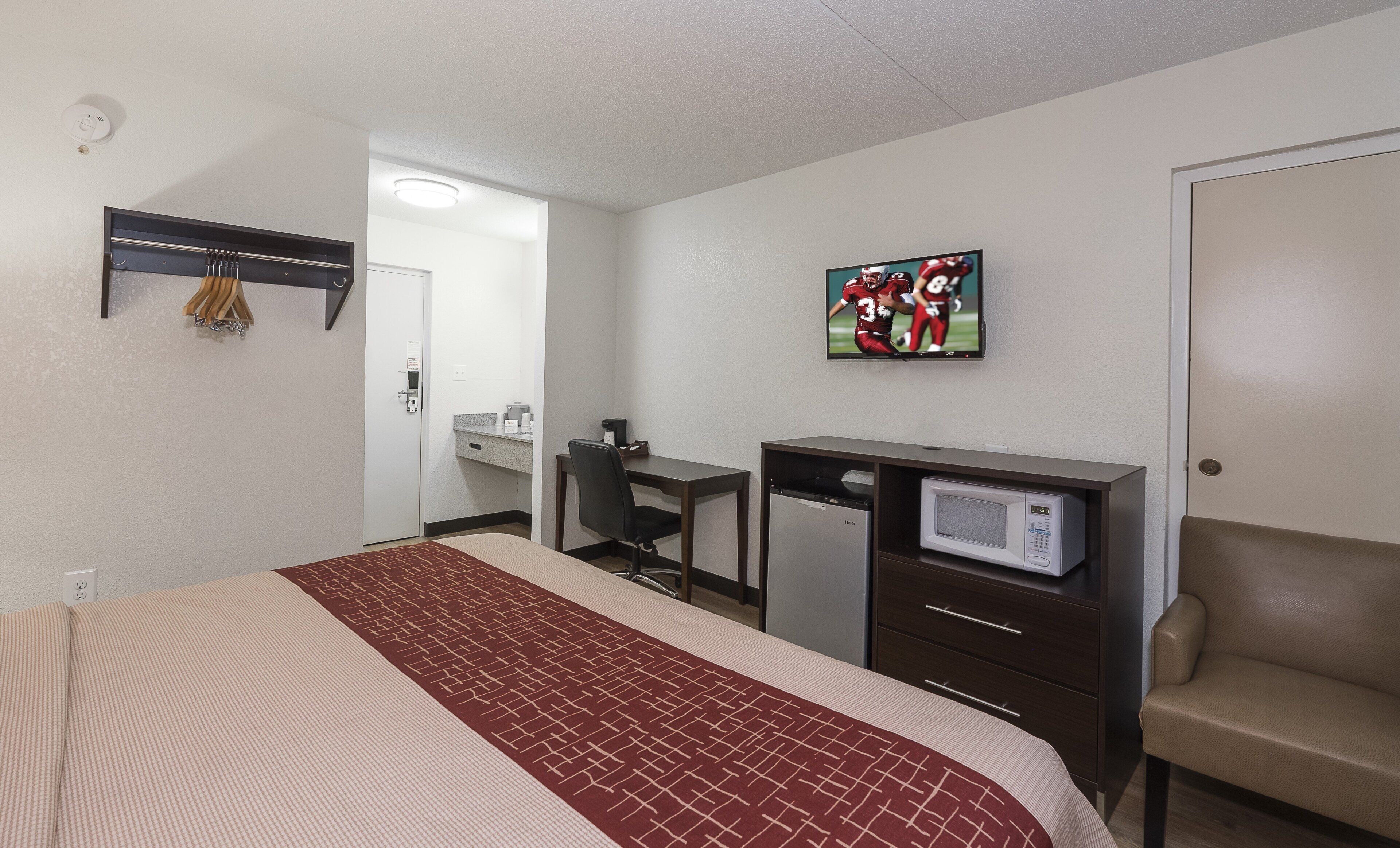 A hotel room with a bed, desk, chair, microwave, and a television on the wall.